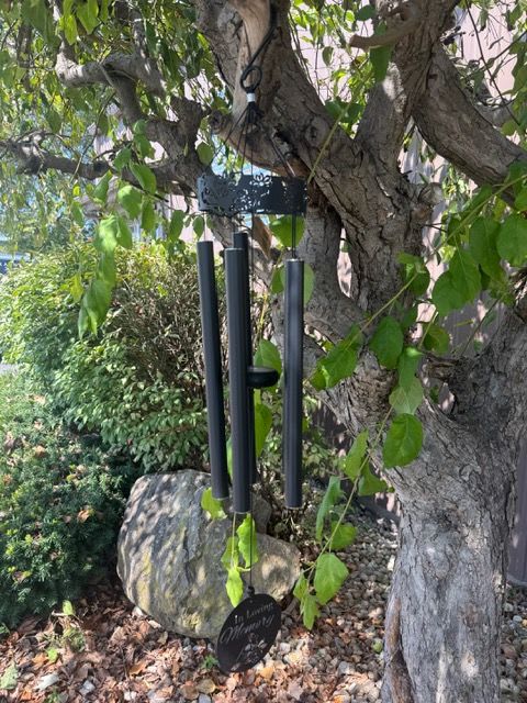 Black wind chimes hanging from a tree branch in a garden