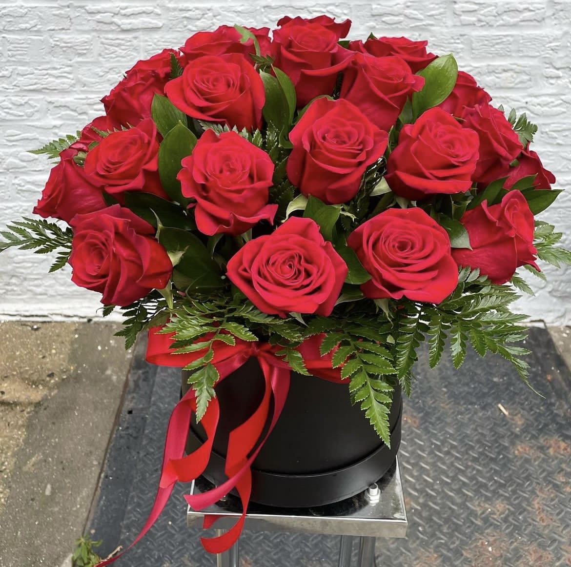 Red roses arranged in a black hatbox with a red ribbon