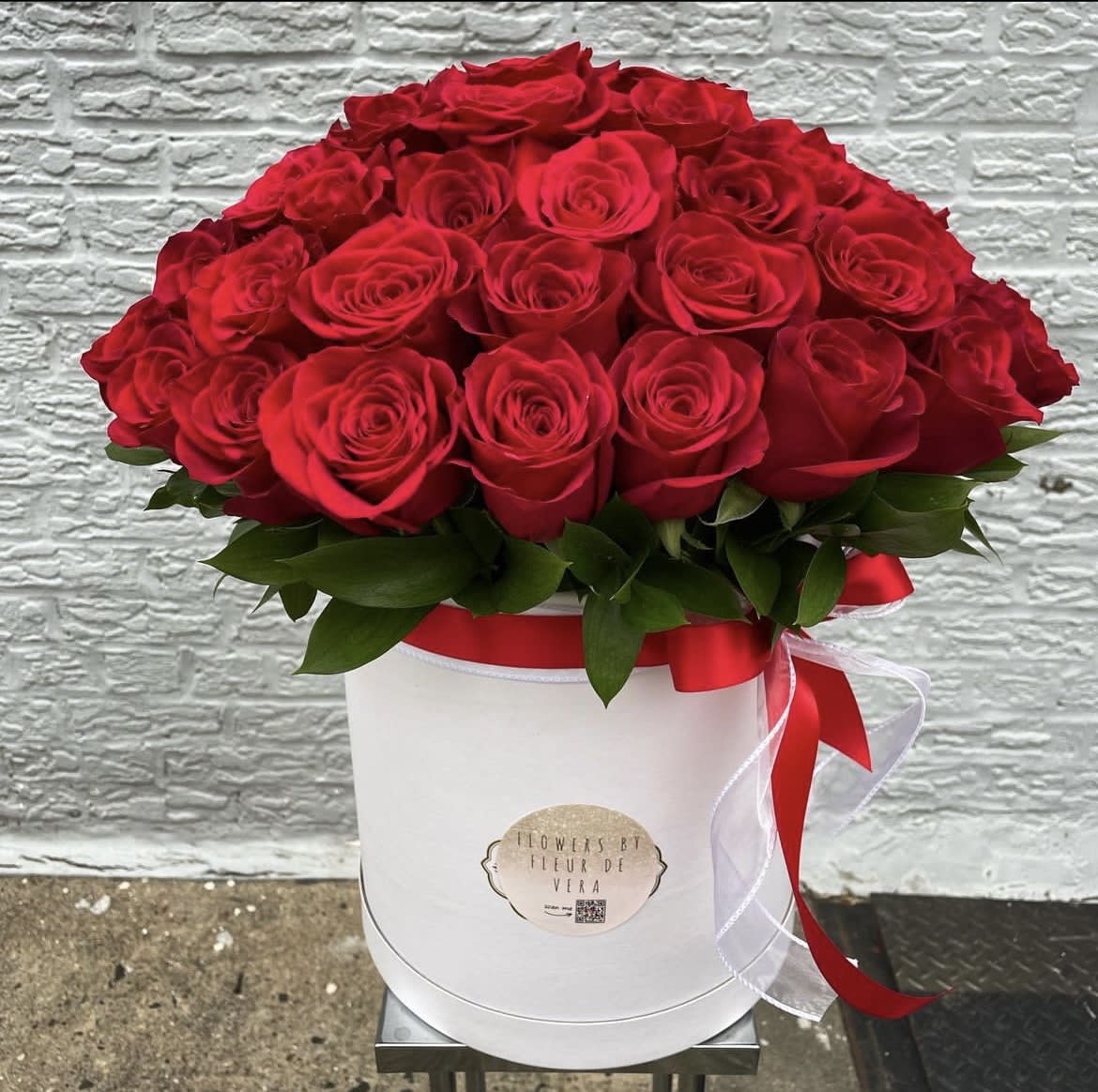 Red roses arranged in a white hat box with a red ribbon