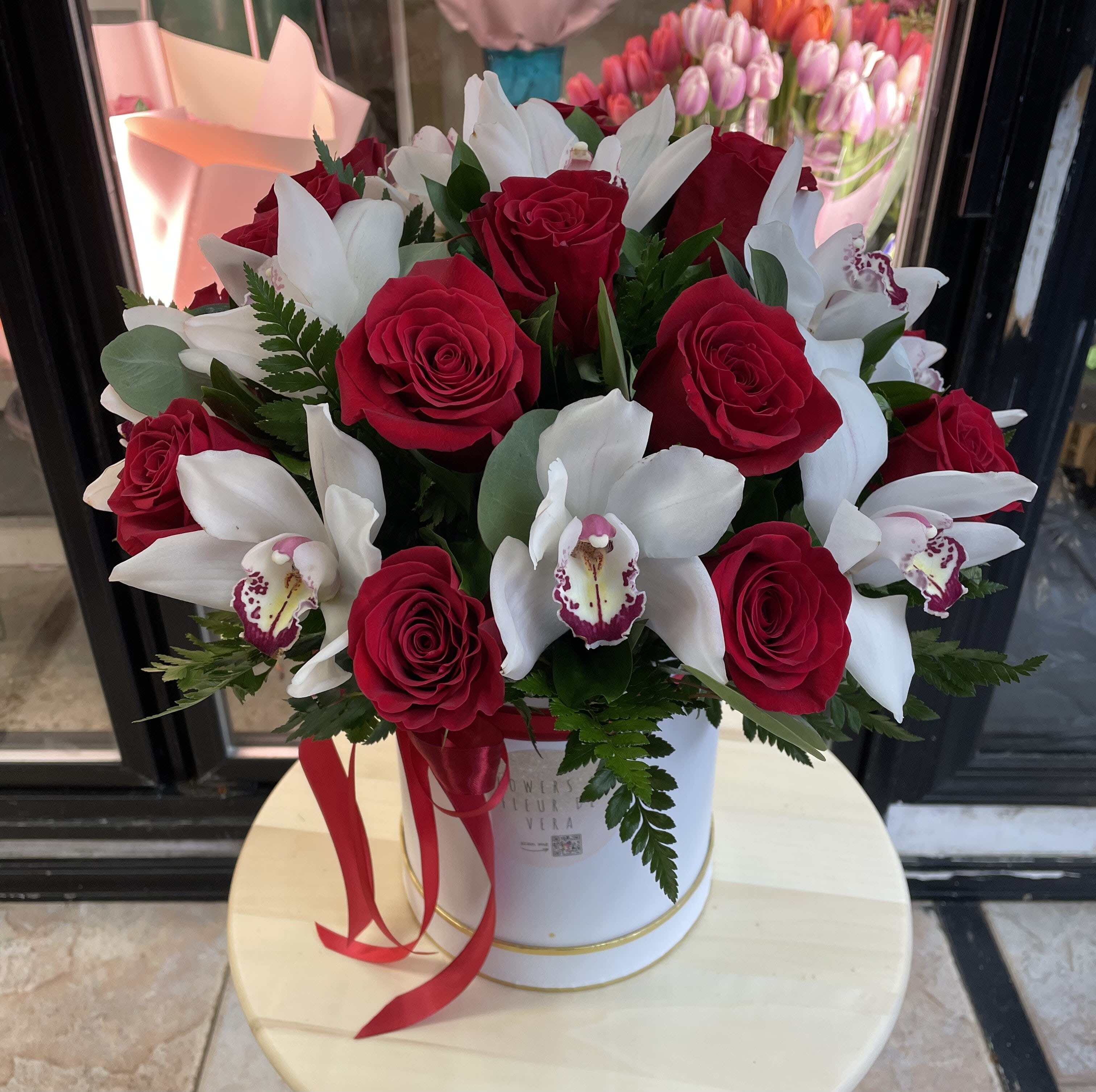 Red roses and white orchids arranged in a white hatbox with a red ribbon