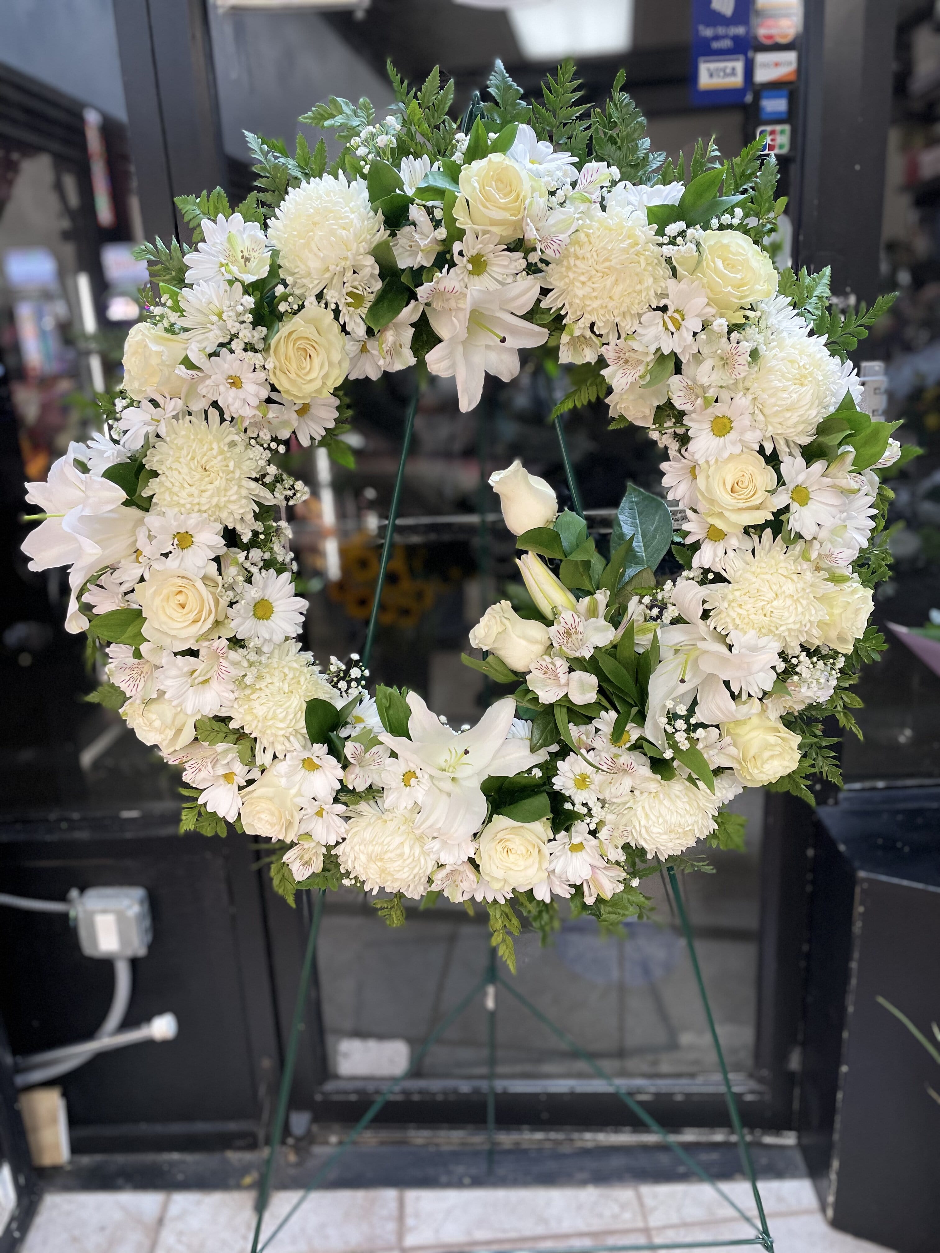 White floral wreath on a stand with roses and daisies