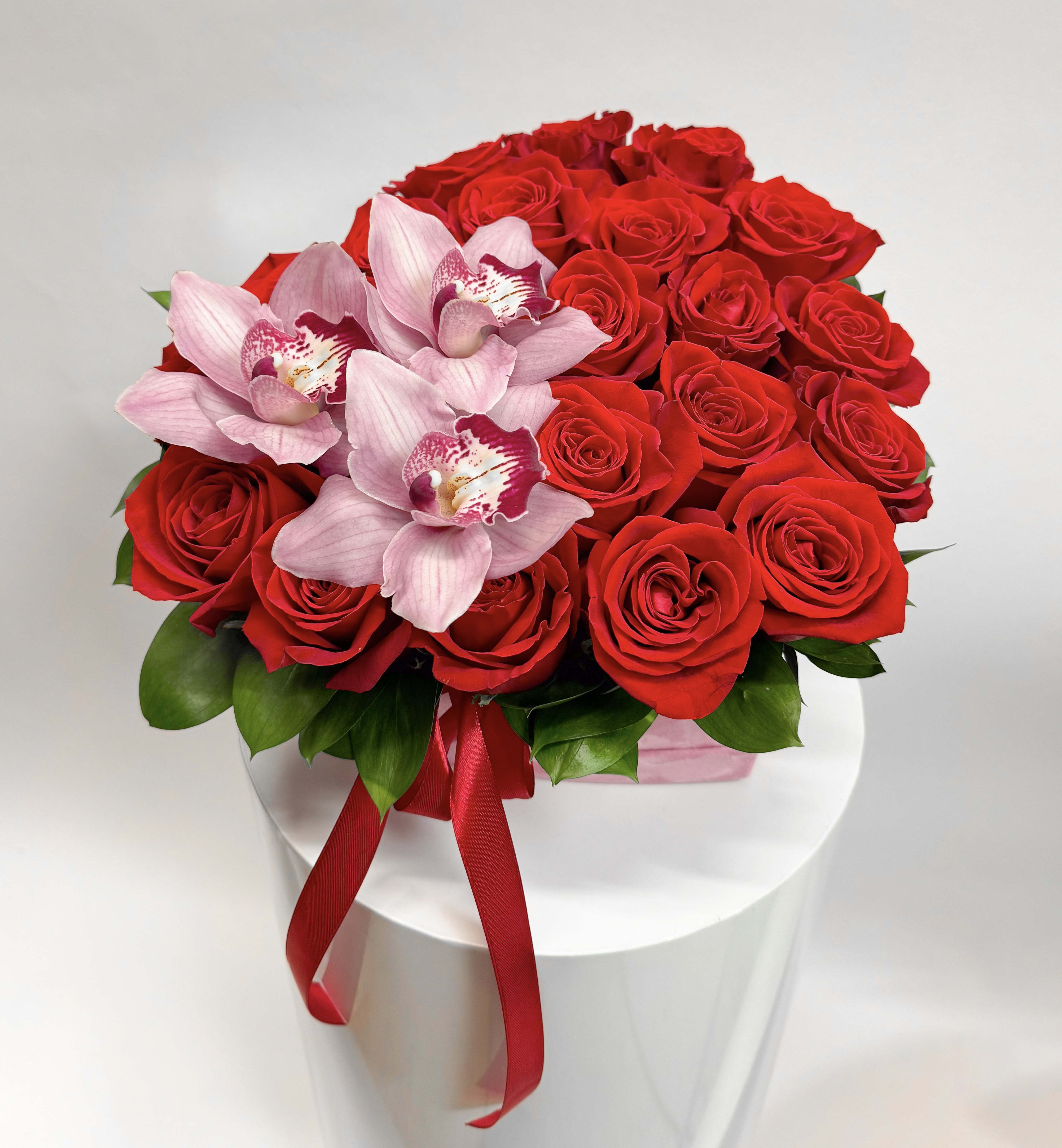 Red roses with pink orchids in a white box tied with a red ribbon