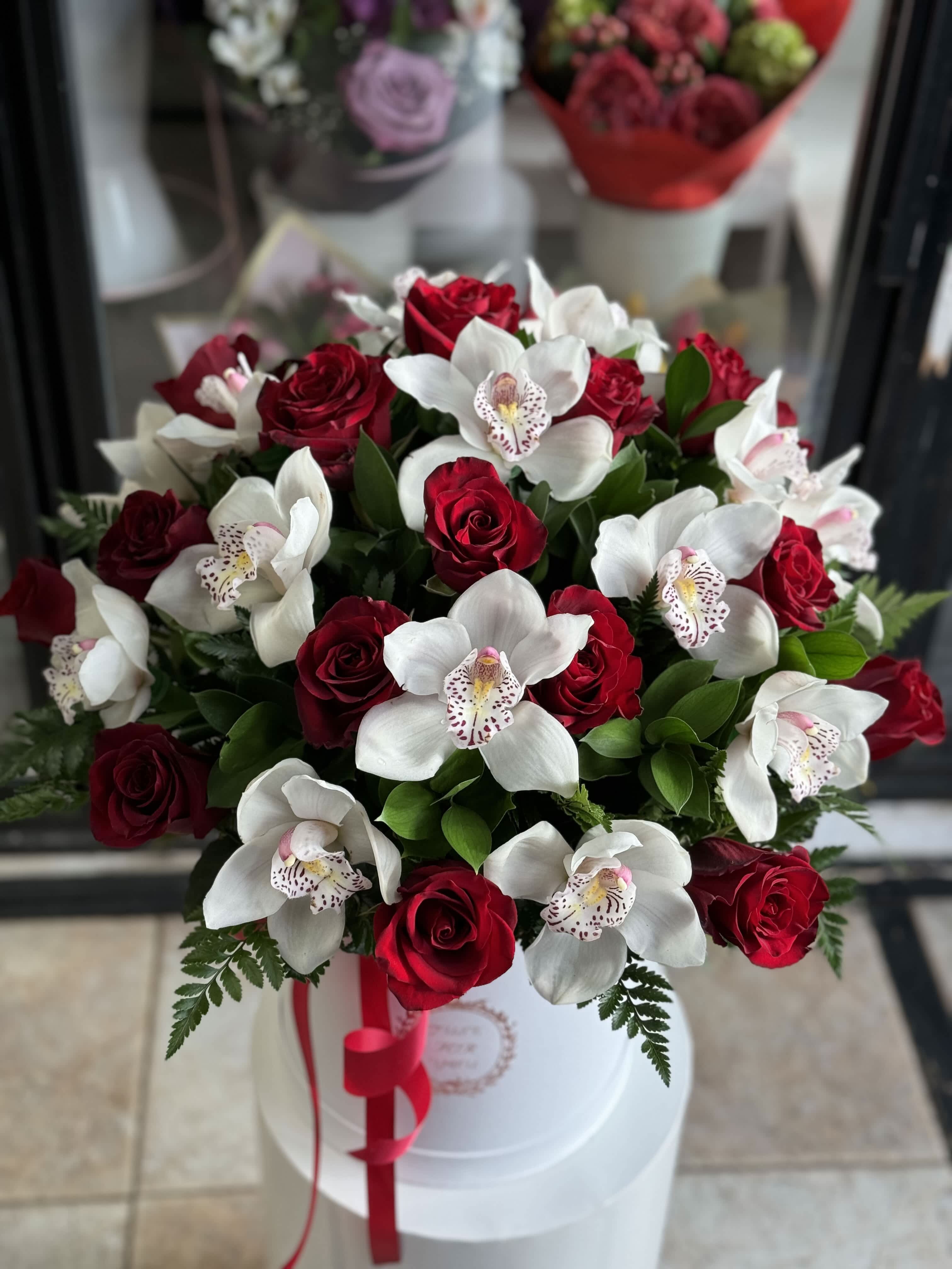 Bouquet of red roses and white orchids in a white hat box with a red ribbon