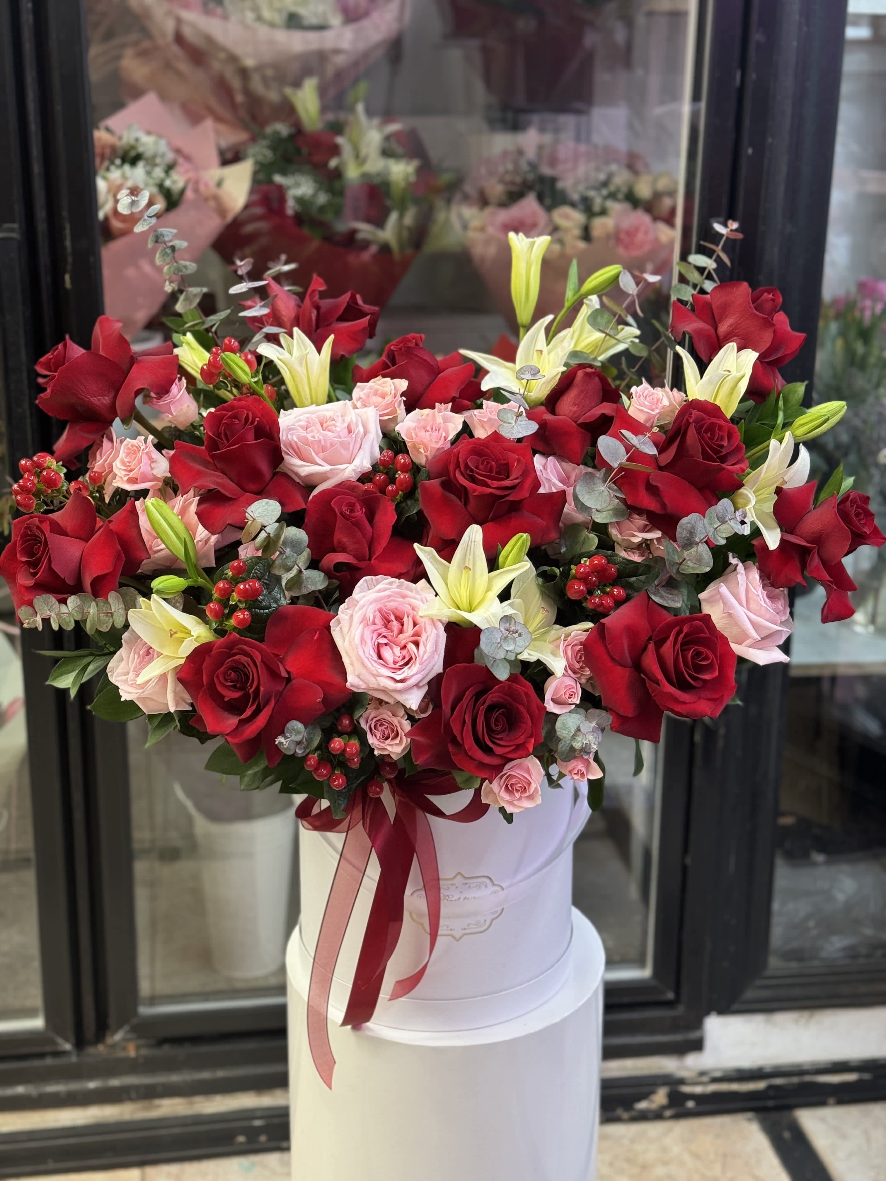 Large bouquet of red and pink roses with white lilies in a white hat box