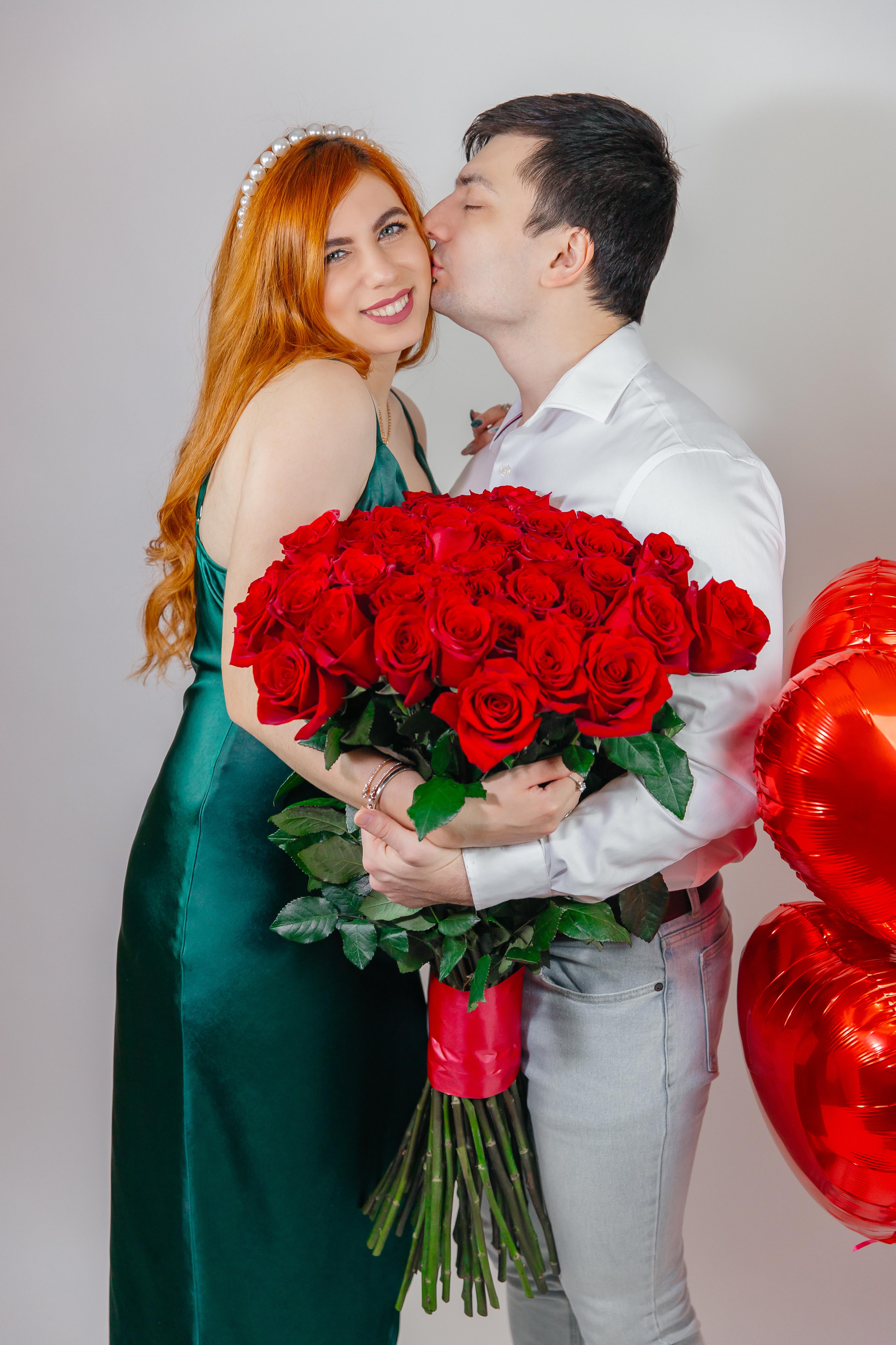 Couple holding a large bouquet of red roses with red heart balloons