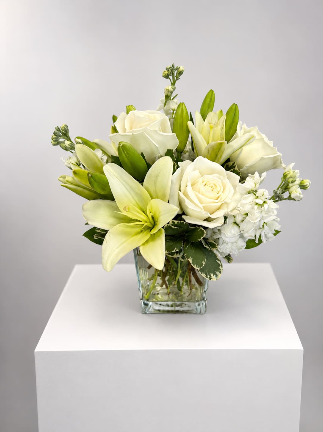 White roses and lilies arranged in a clear glass vase
