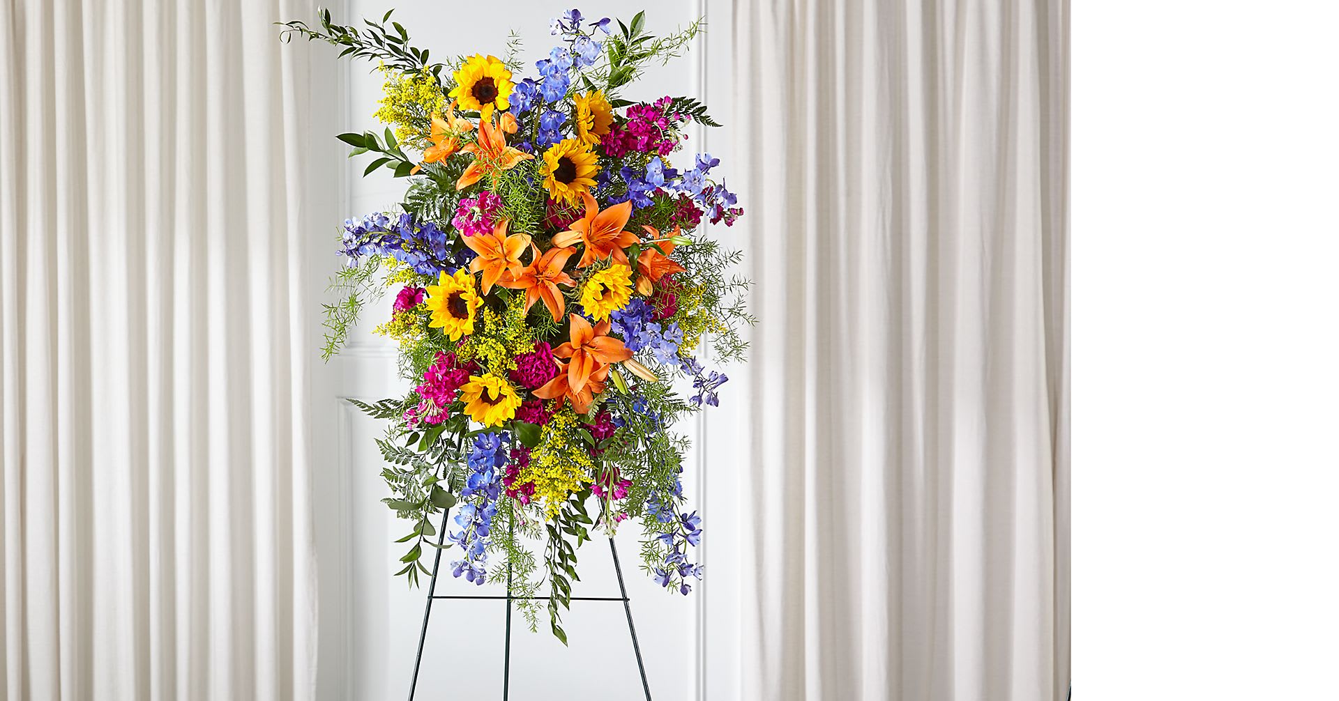 Tall standing floral spray with sunflowers, lilies, and blue flowers