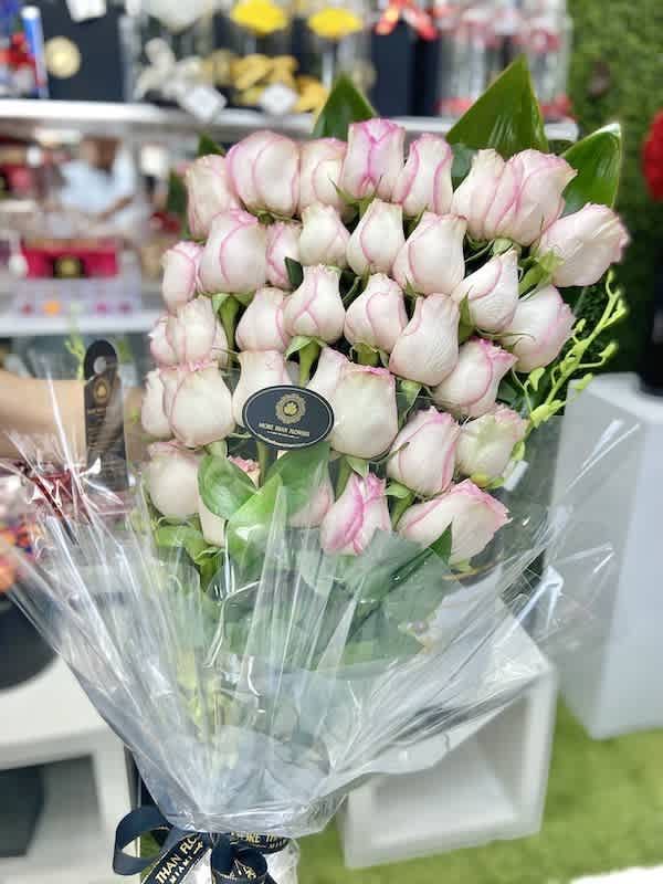 Tall bouquet of white roses with pink edges wrapped in clear cellophane with a black ribbon