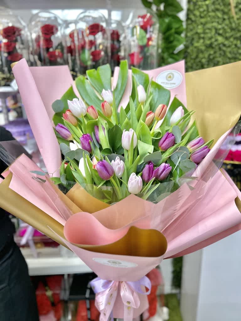 Hand-tied bouquet of pink, purple, and white tulips wrapped in pink and gold paper with a ribbon