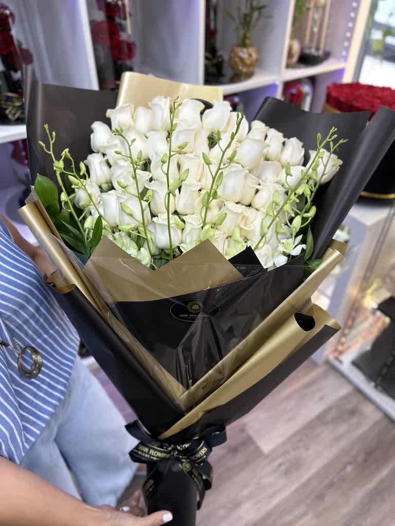 Tall bouquet of white roses with green orchid buds wrapped in black and gold paper