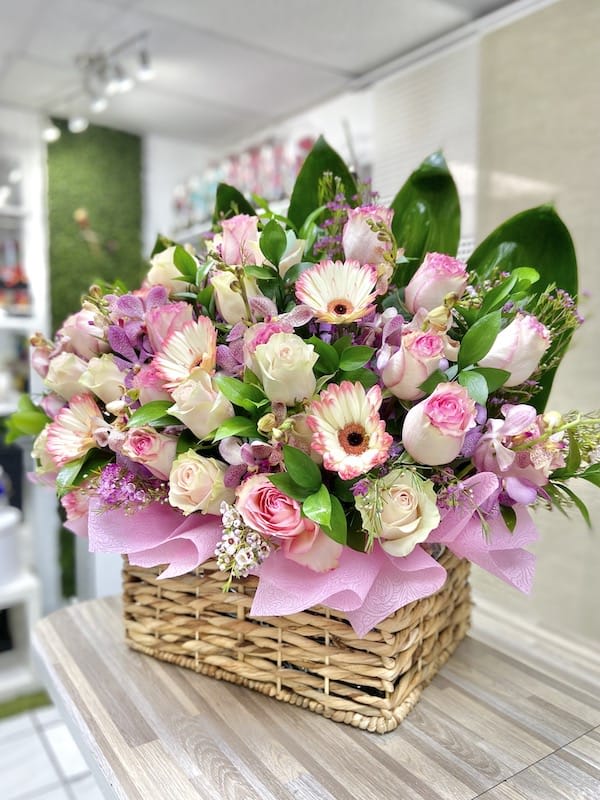 Low basket arrangement of pink gerbera daisies and roses with white accent flowers