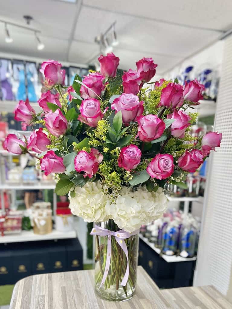 Tall vase arrangement of hot pink roses and white hydrangeas tied with a ribbon