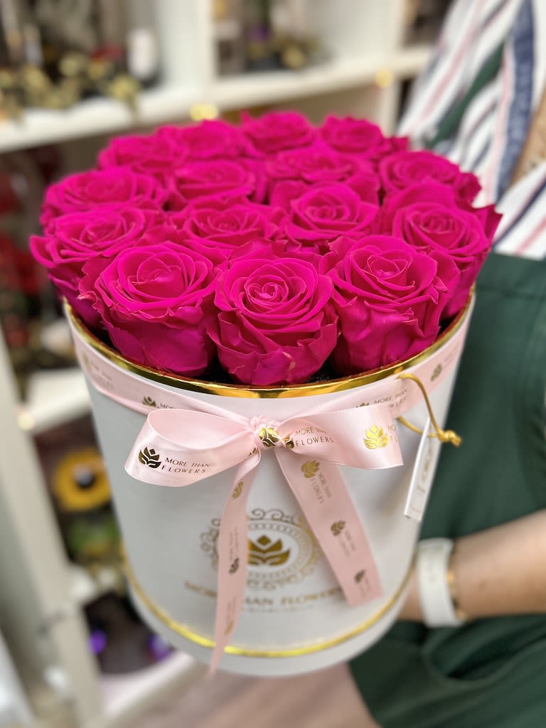 Round white hatbox filled with bright fuchsia roses and tied with a pink ribbon.