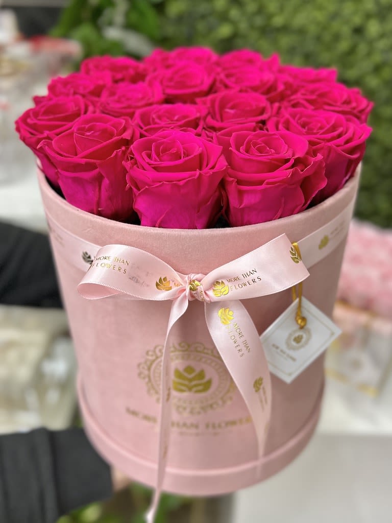 Hot pink roses arranged tightly in a round pink hat box with ribbon and logo