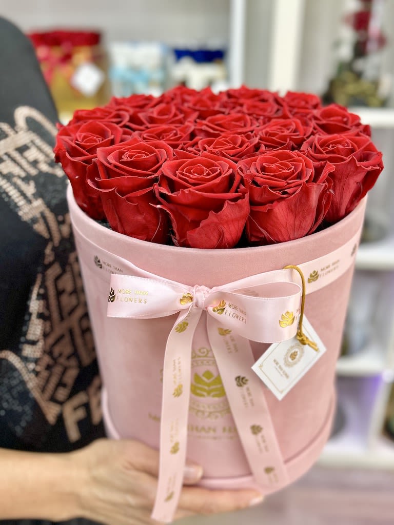 Round box of red roses in a pink hatbox with ribbon and tag