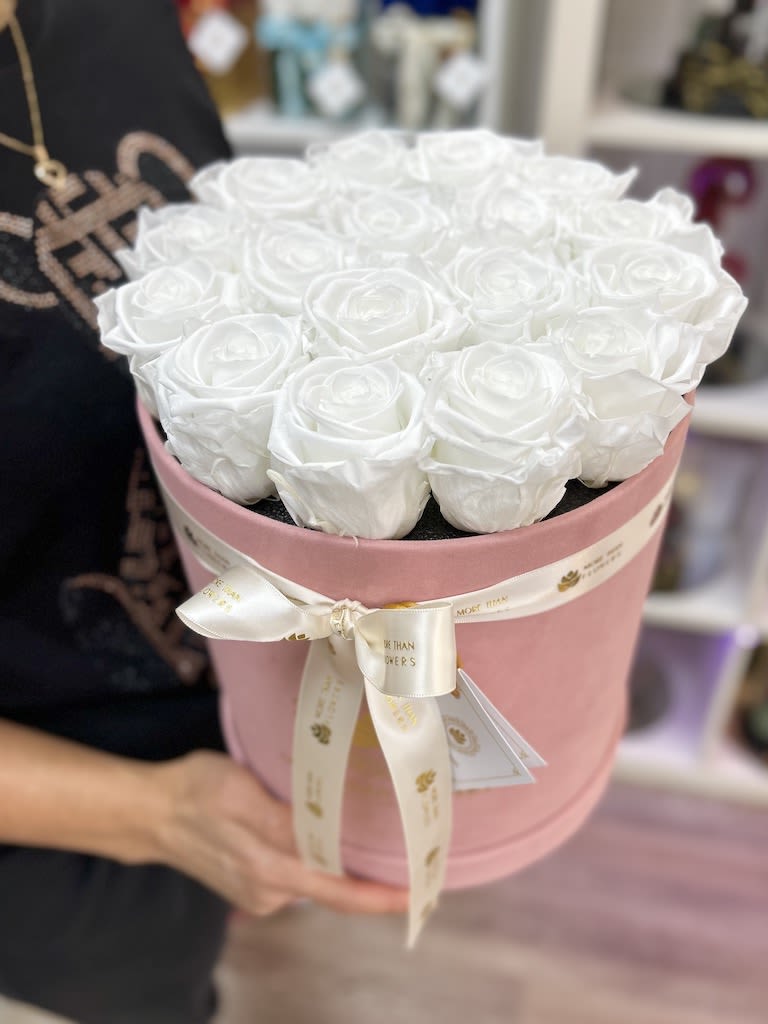 Round pink hatbox packed with white roses and tied with an ivory ribbon.