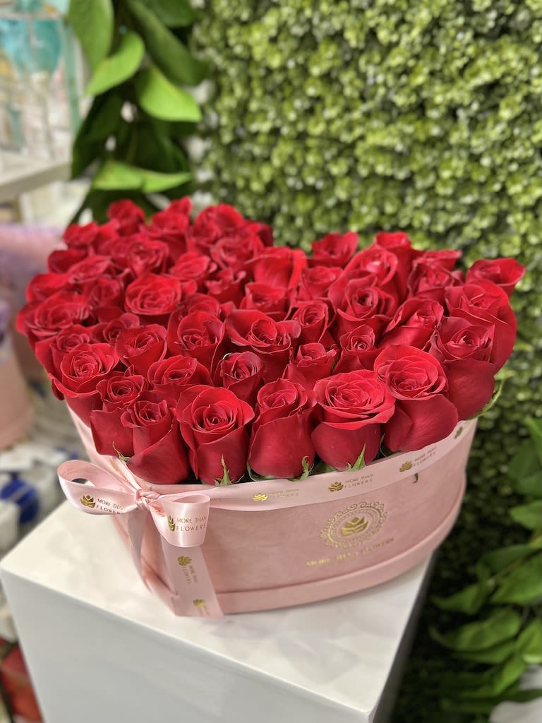 Heart-shaped pink hatbox filled with tightly packed red roses and tied with a pink ribbon