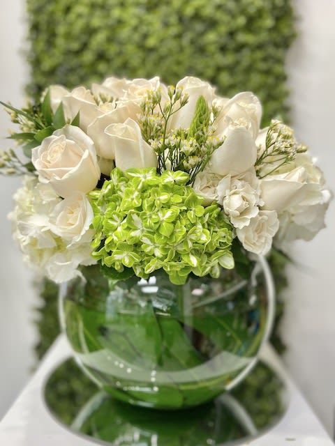 Low arrangement of white roses and green hydrangea in a round glass bowl vase