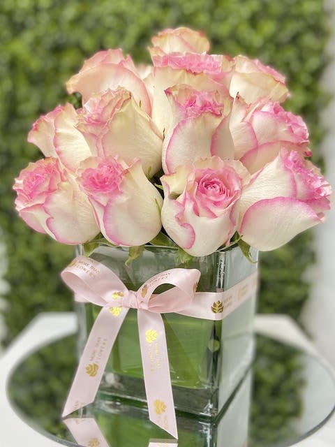 Compact arrangement of white roses edged in pink in a square glass vase with a pink ribbon bow