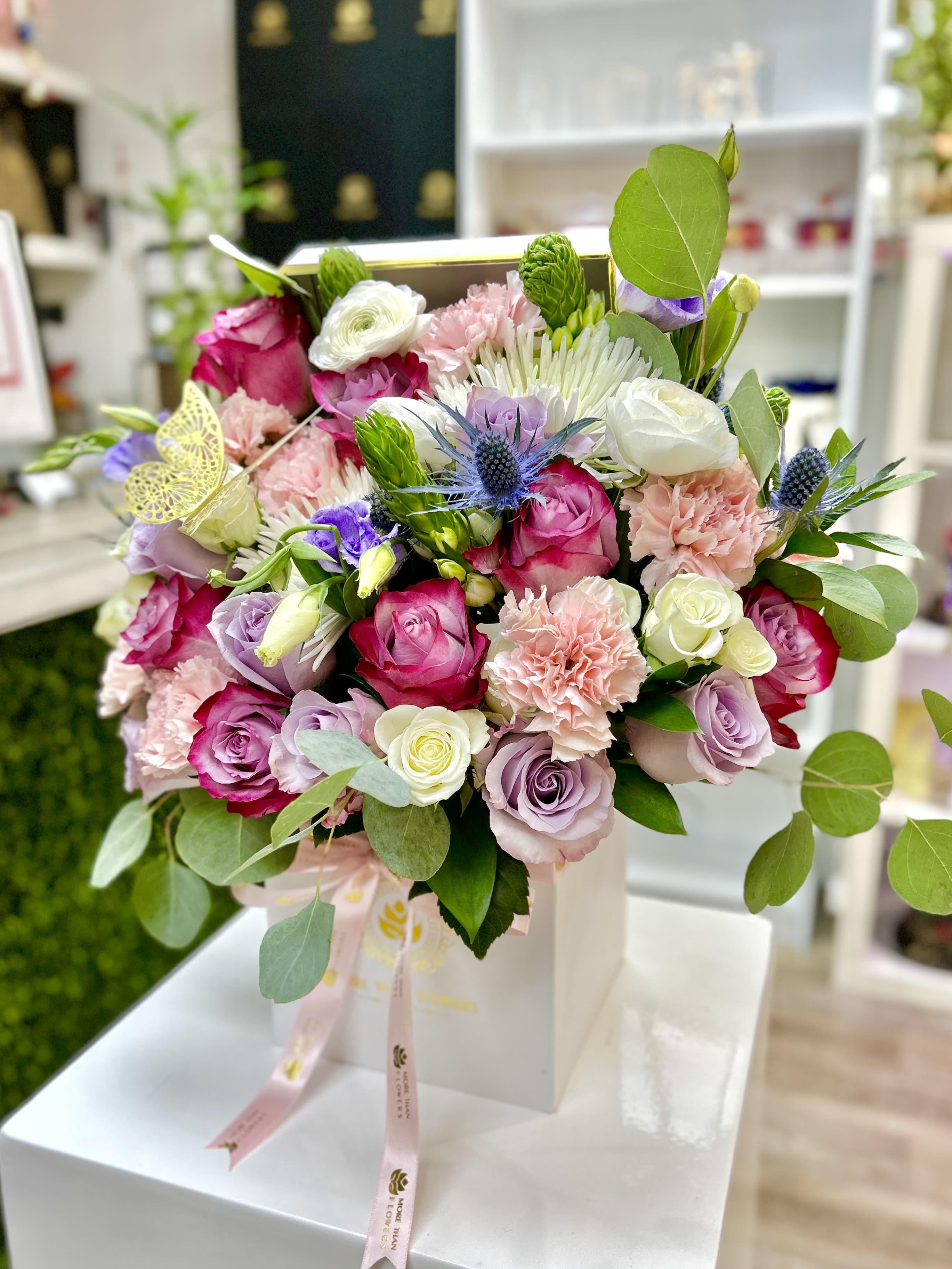 Pink, white, and lavender rose and carnation arrangement in a white box with ribbon and butterfly accent