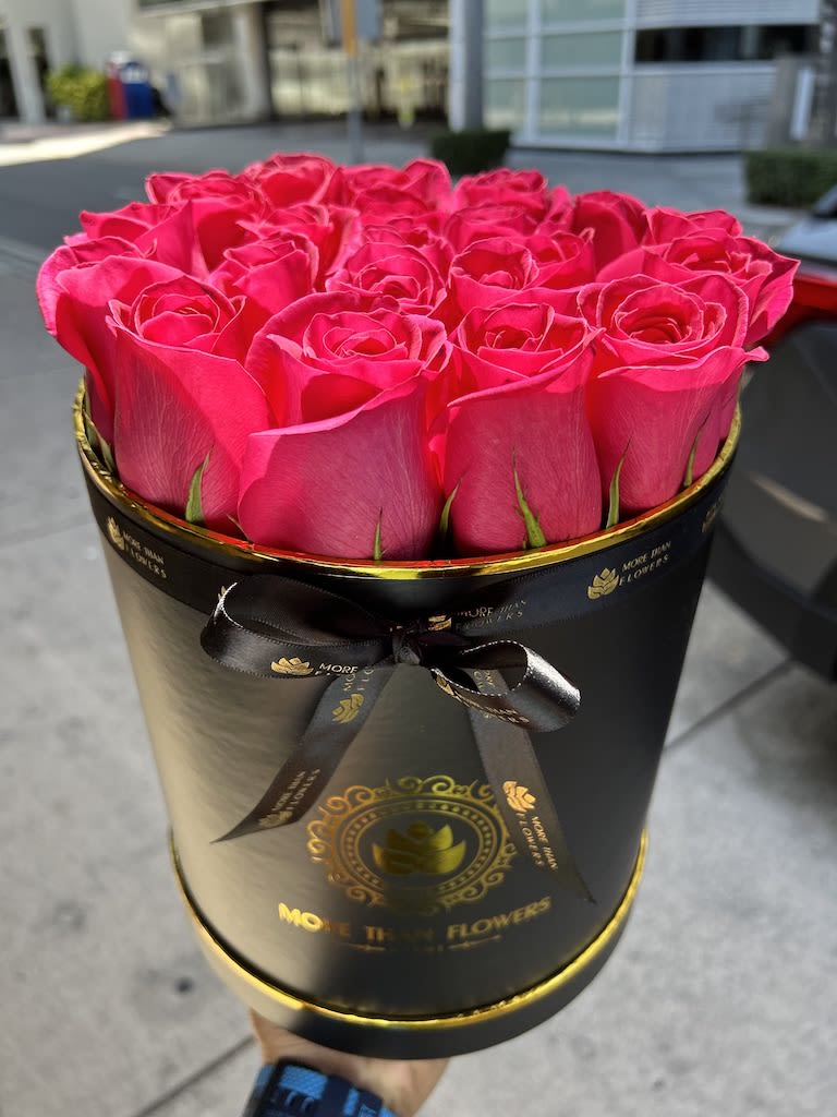 Bright pink roses arranged in a round black hatbox with gold accents and ribbon