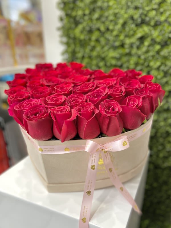 Box of red roses arranged tightly in a beige hat box with a pink ribbon bow