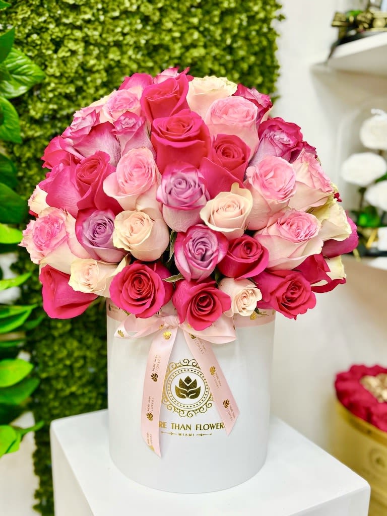 Round hat box arrangement of pink, cream, and lavender roses in a white cylinder box with ribbon.