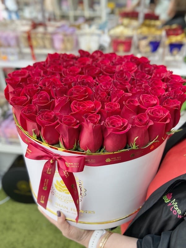 Large round box filled with tightly packed red roses, wrapped with a red ribbon