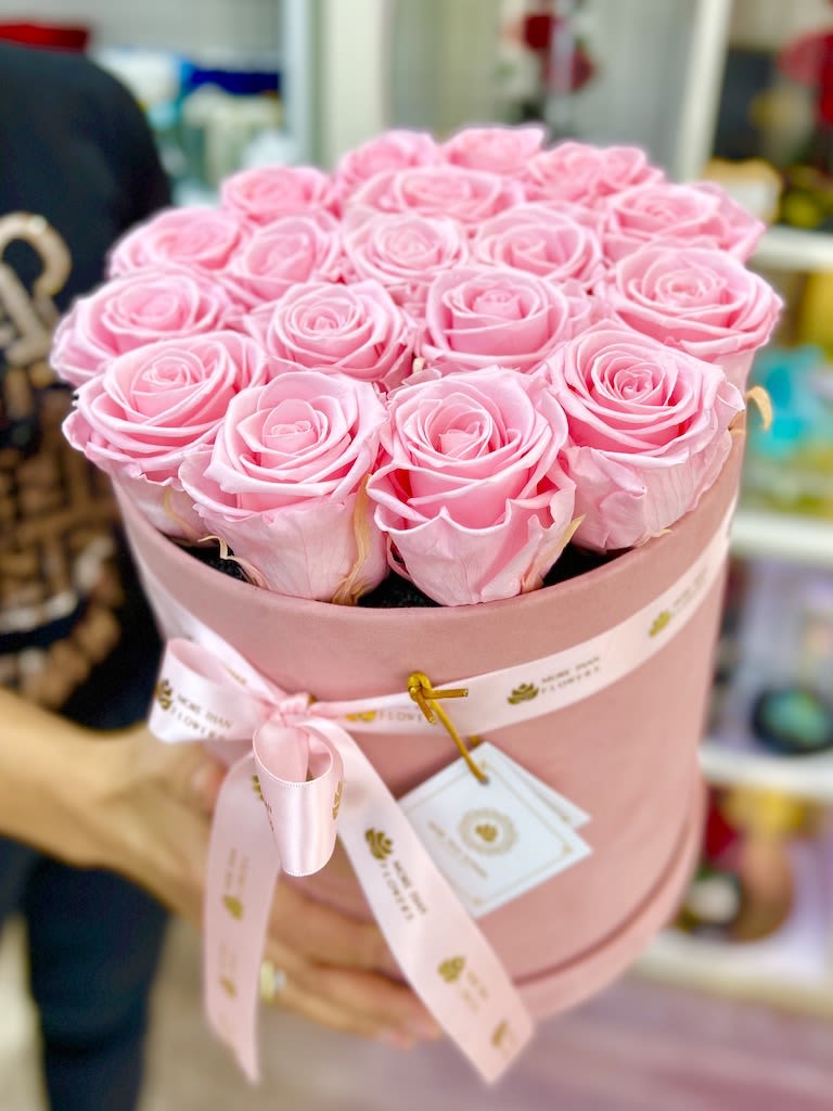 Pink hat box filled with tightly packed light pink roses and tied with a matching ribbon