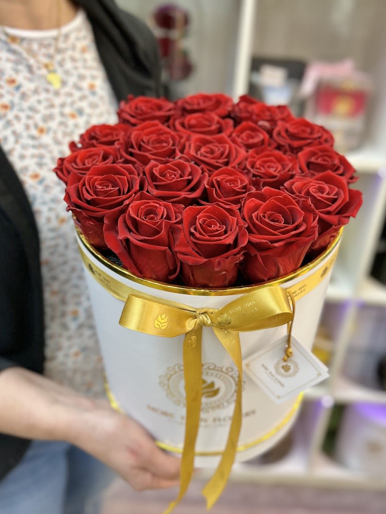 Round white hat box filled with tightly packed red roses and tied with a gold ribbon