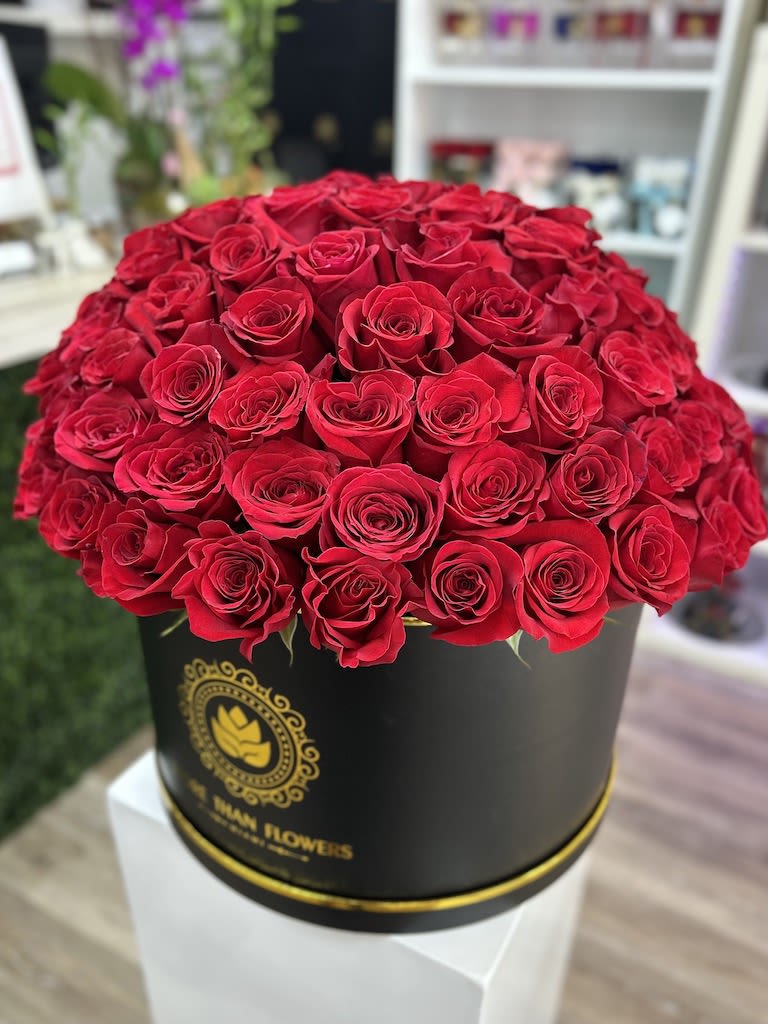 Round black hatbox filled with many red roses on a white pedestal.