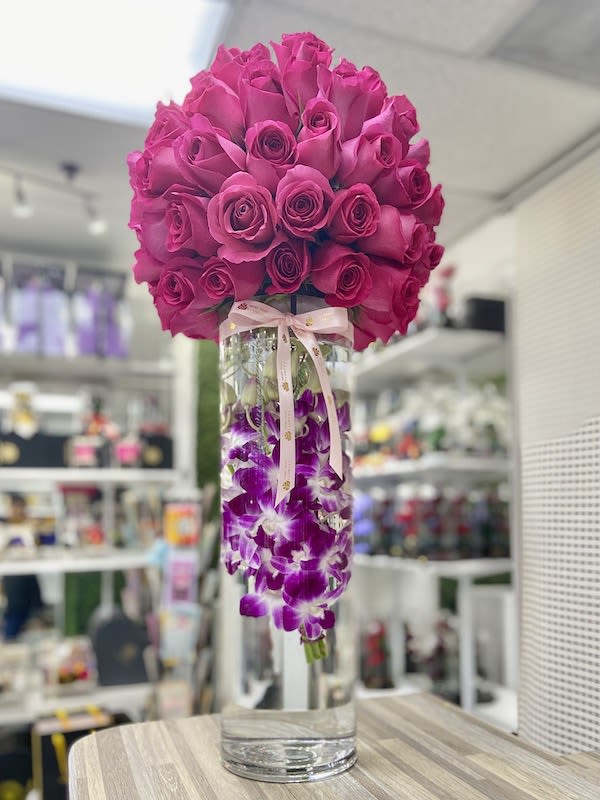 Tall glass vase with hot pink roses on top and submerged purple orchids tied with a ribbon.