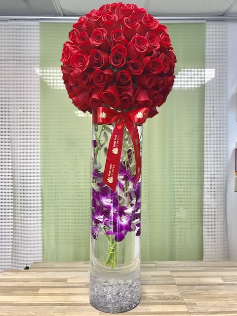 Tall glass vase with submerged purple orchids topped by a large red rose sphere and red ribbon