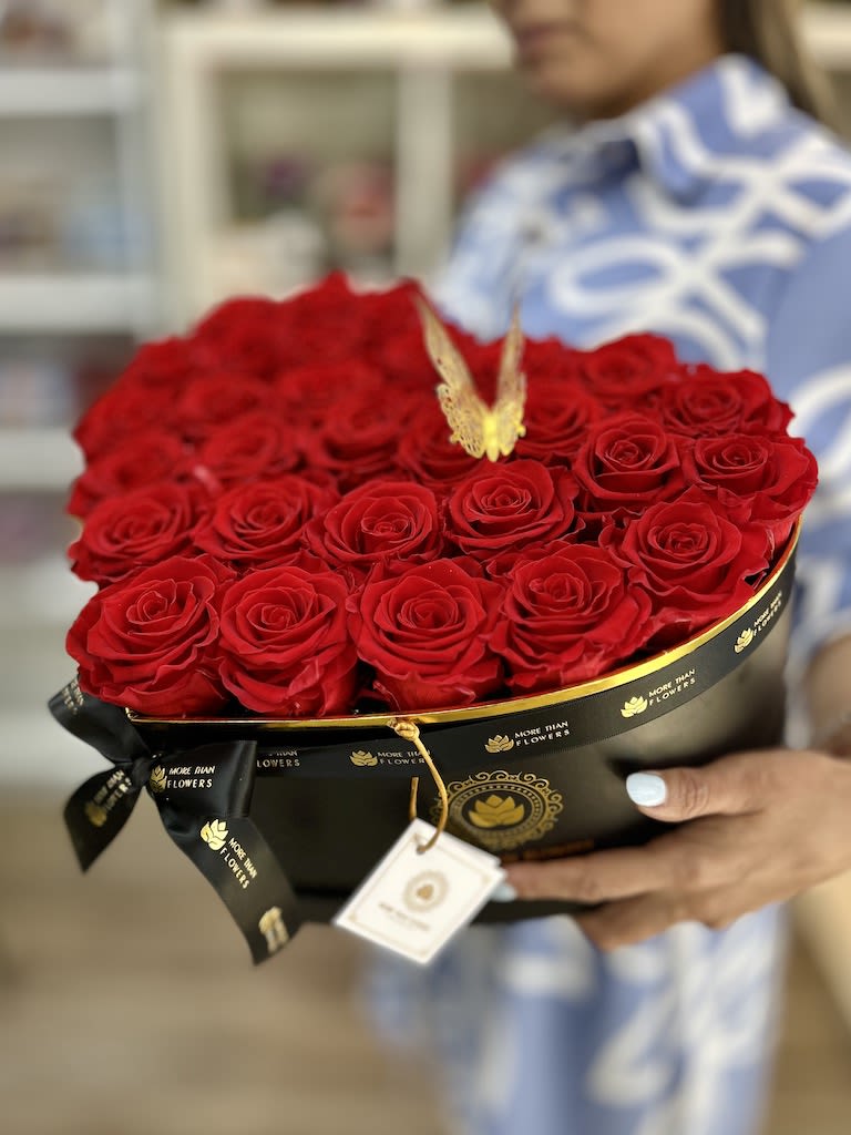 Heart-shaped black box filled with red roses and a gold butterfly accent, held in someone’s hands.