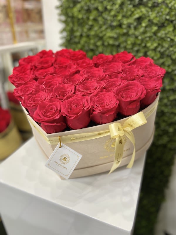 Heart-shaped beige box filled with red roses and tied with a yellow ribbon