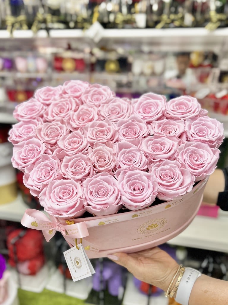 Heart-shaped arrangement of light pink roses in a pink hat box with ribbon.