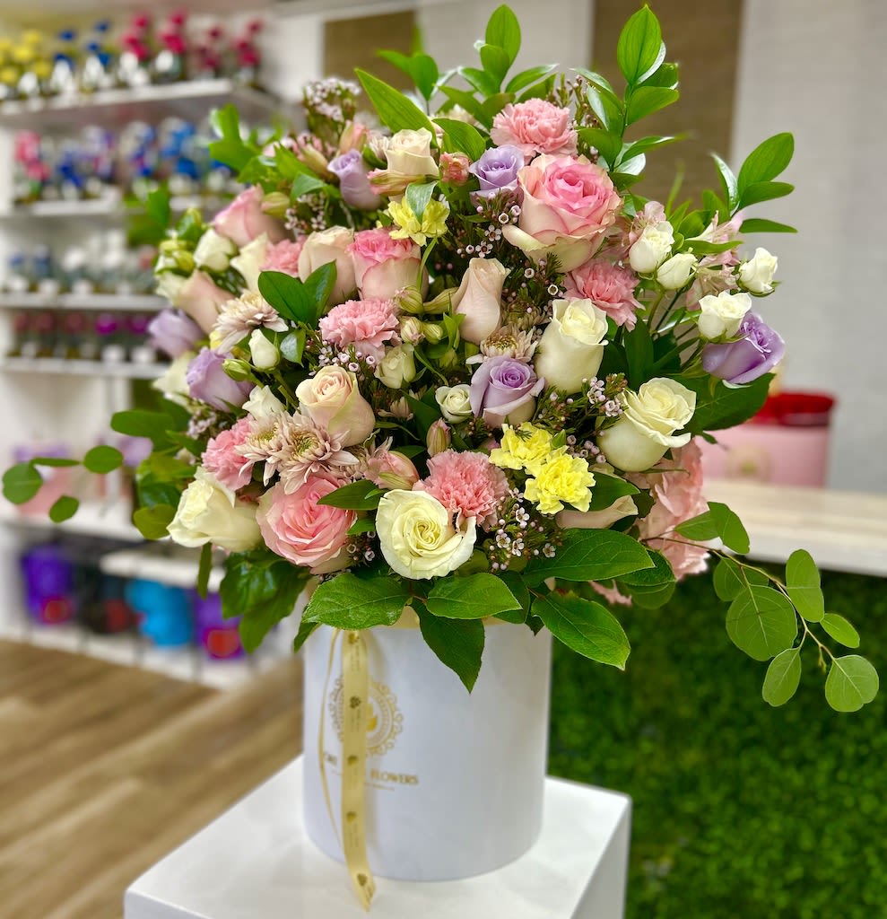 Pastel arrangement of roses, carnations, and mums in a white hat box-style container.