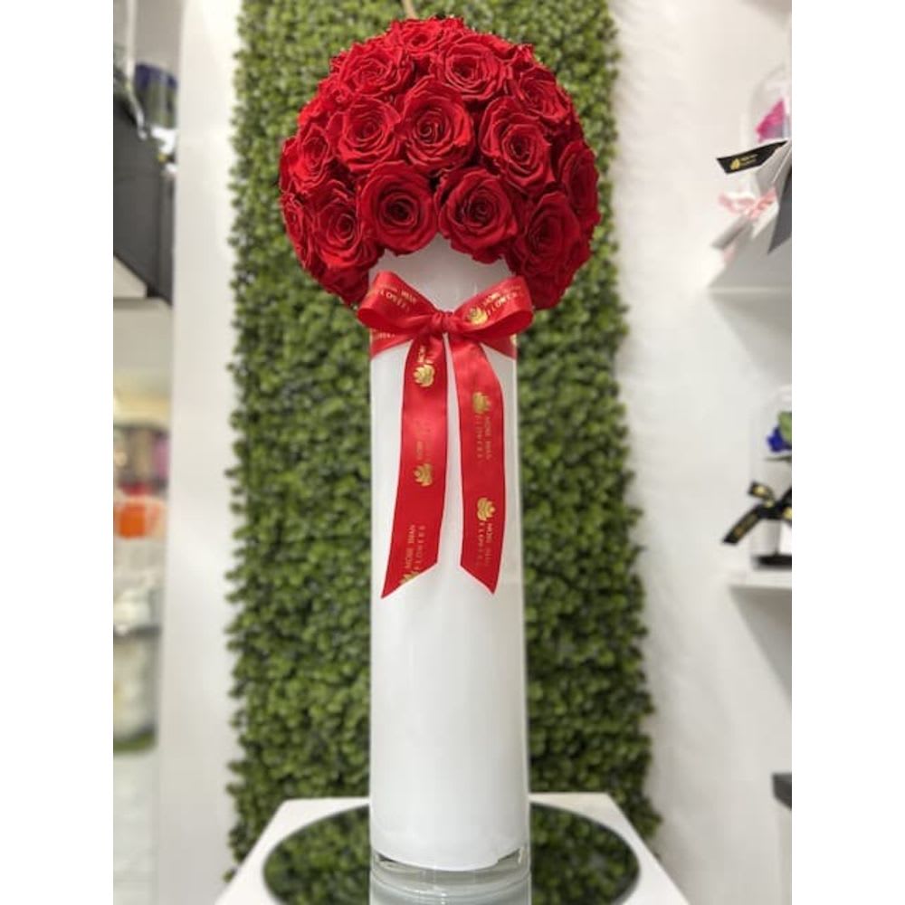 Tall white cylinder vase topped with a dome of red roses and a red bow