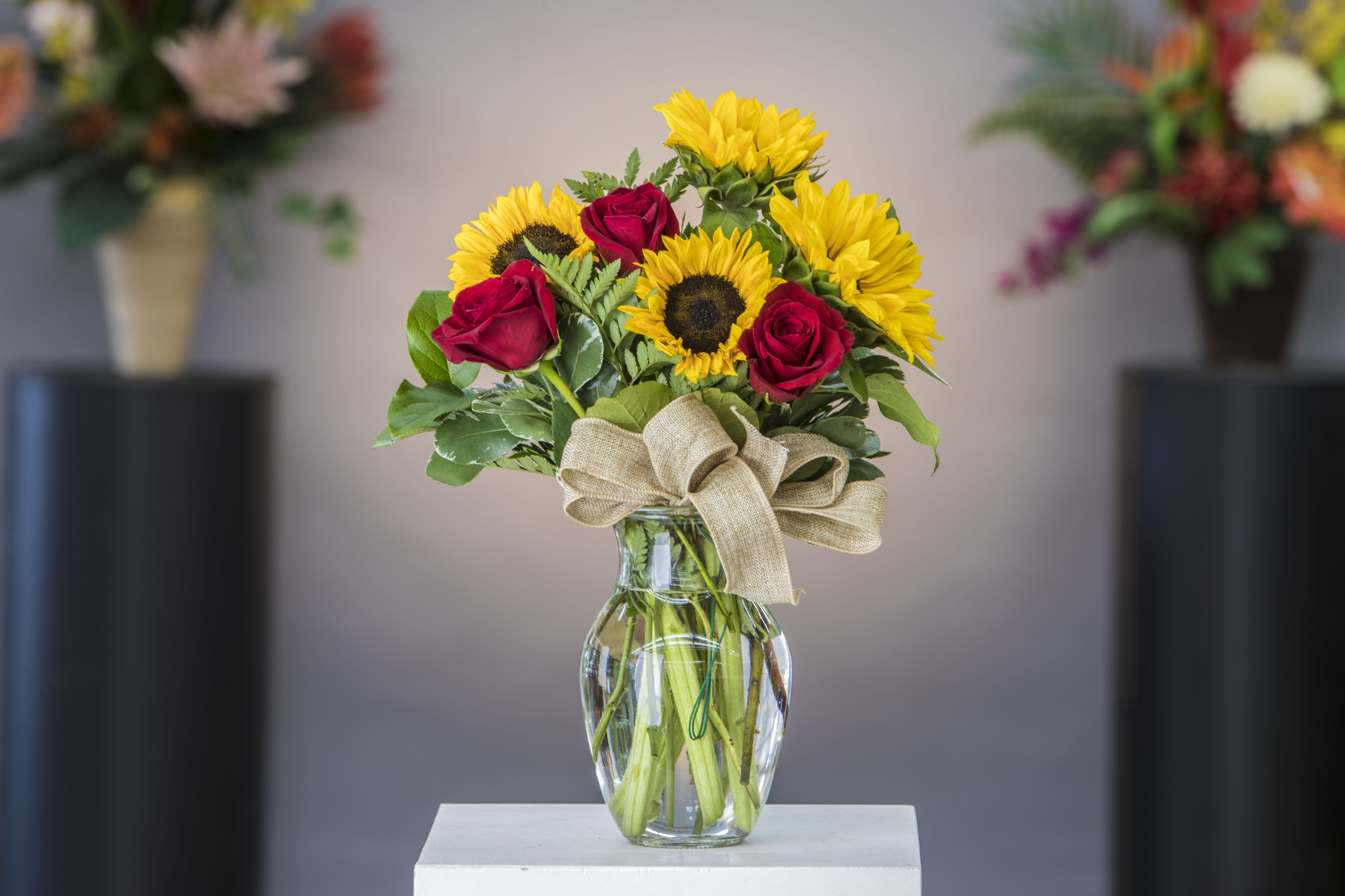 Sunflowers and red roses in a clear glass vase with a burlap bow