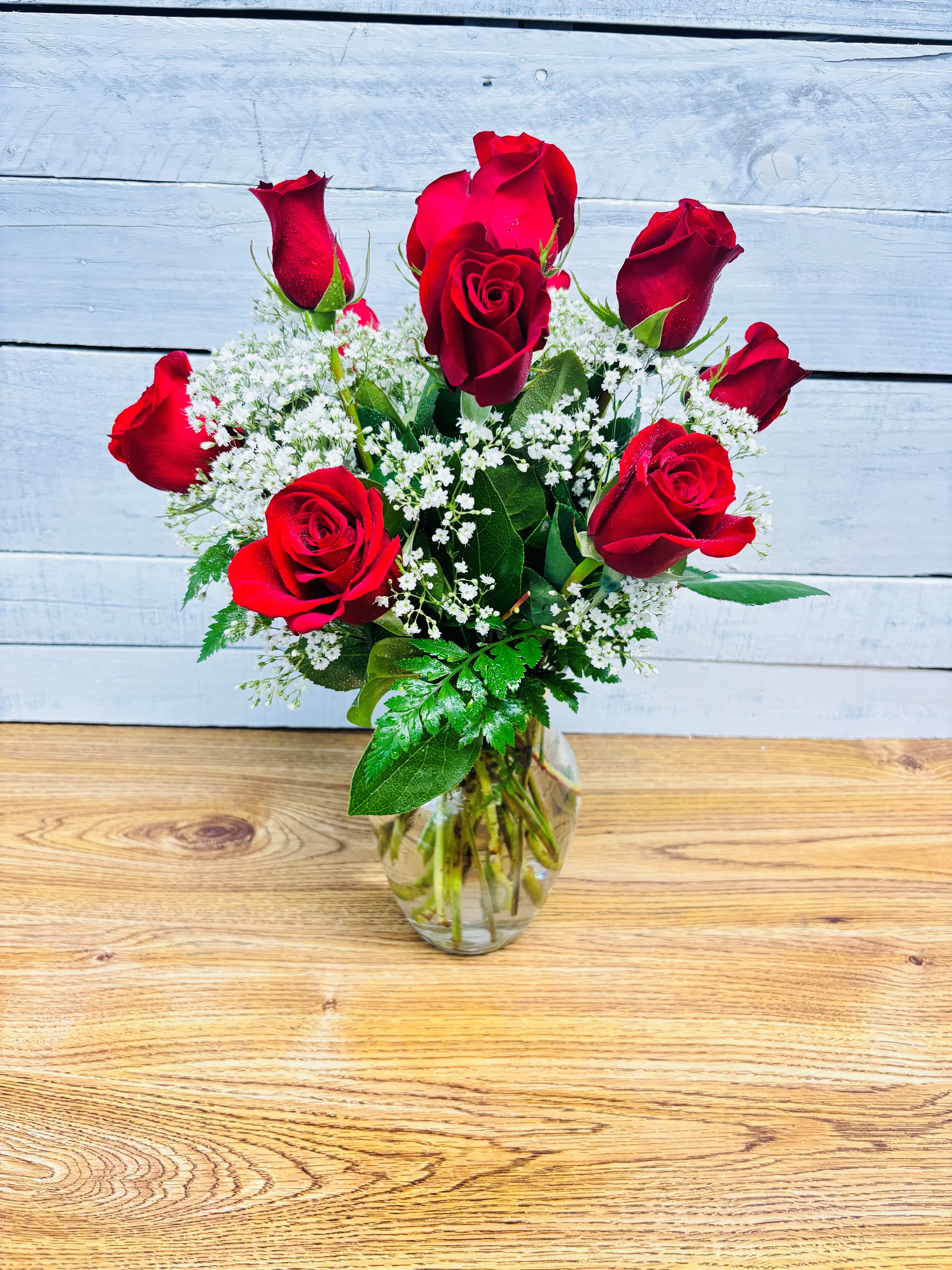Red roses arranged in a clear glass vase with white filler flowers