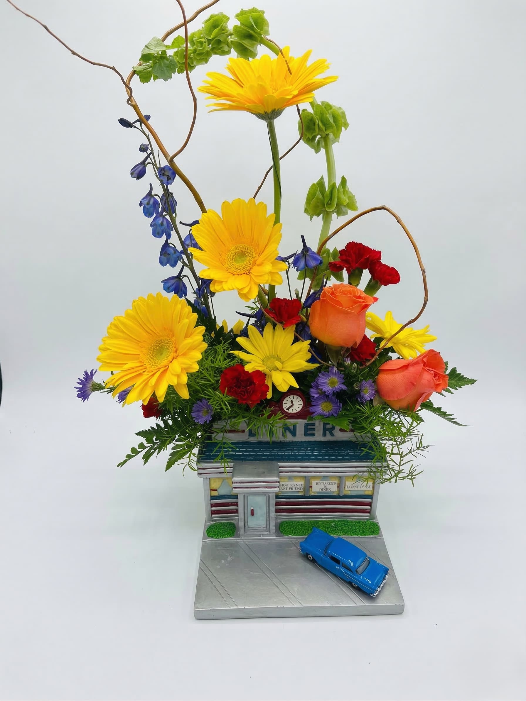 Colorful flower arrangement in a diner-shaped container with a blue toy car