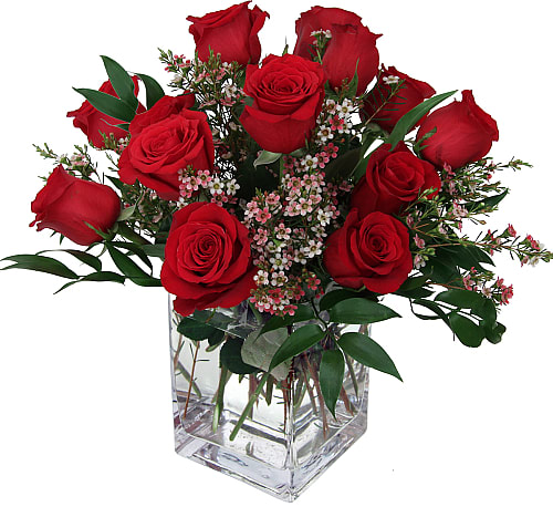 Red roses arranged in a clear square glass vase with small pink filler flowers