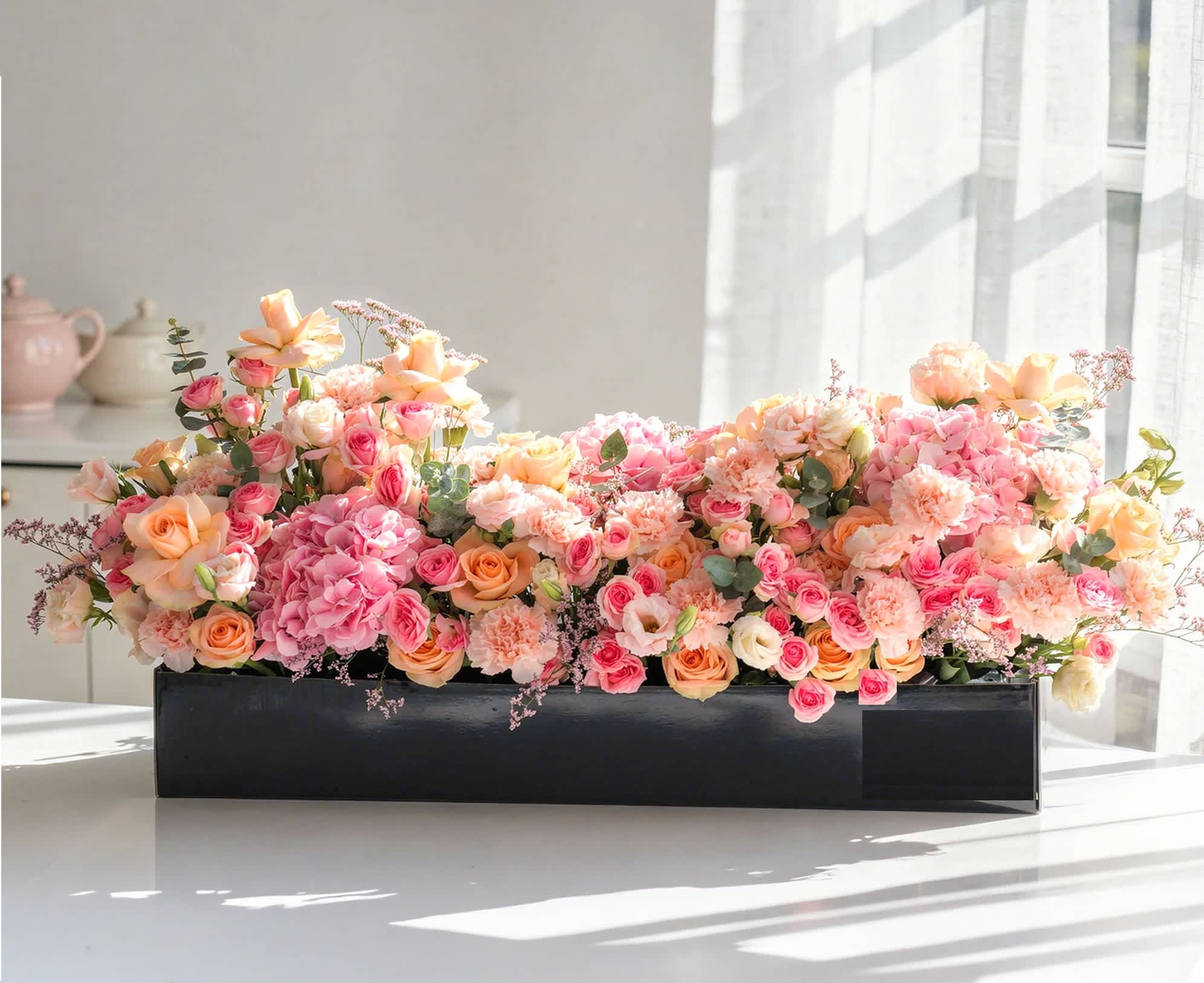 Low rectangular flower arrangement in a black box with pink and peach blooms