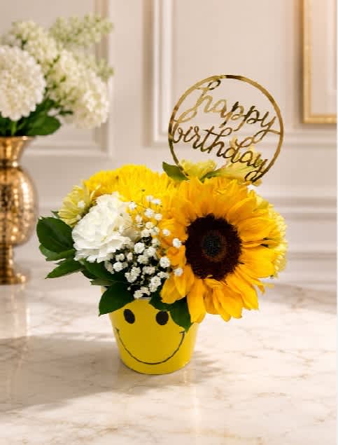 Sunflower and white flower arrangement in a yellow smiley-face pot with a birthday topper
