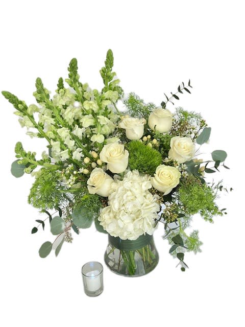 White roses and hydrangea in a glass vase with a small candle