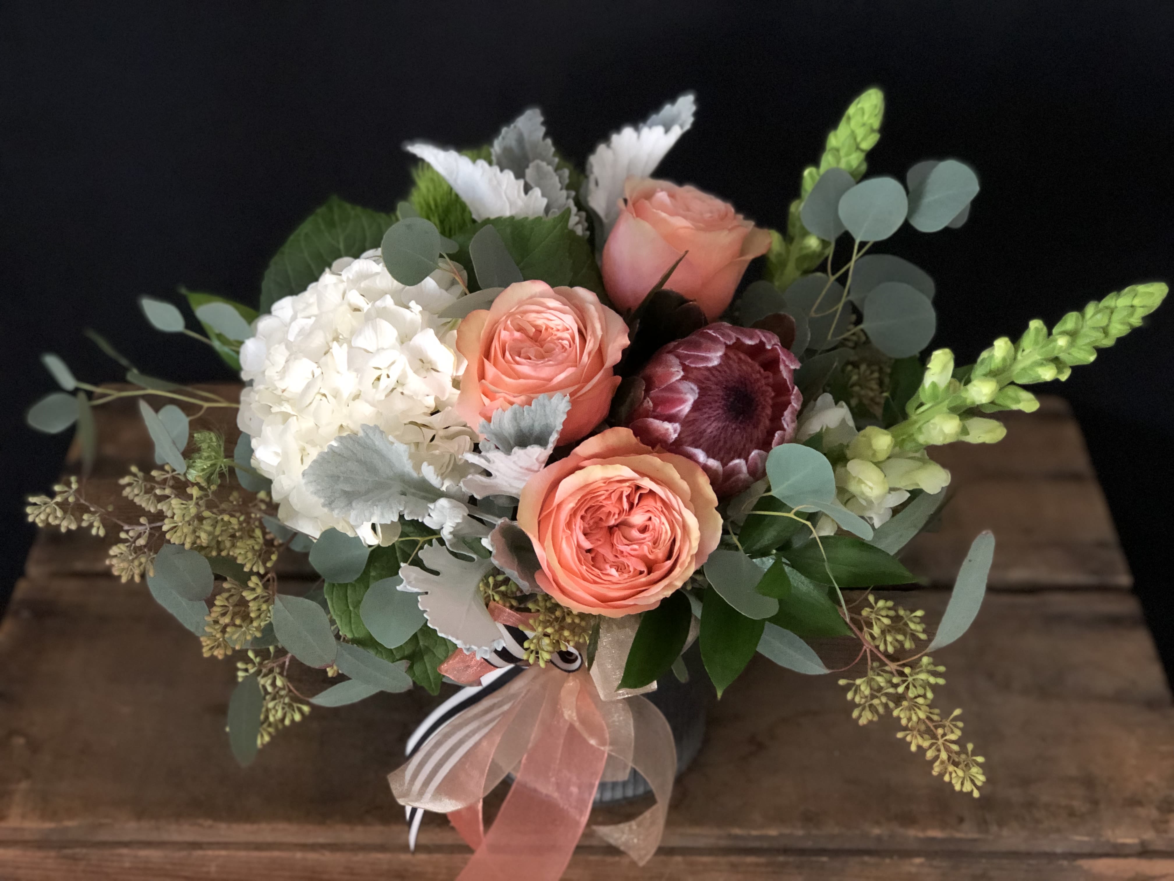 Bouquet of peach roses, white hydrangea, and mixed greenery in a vase