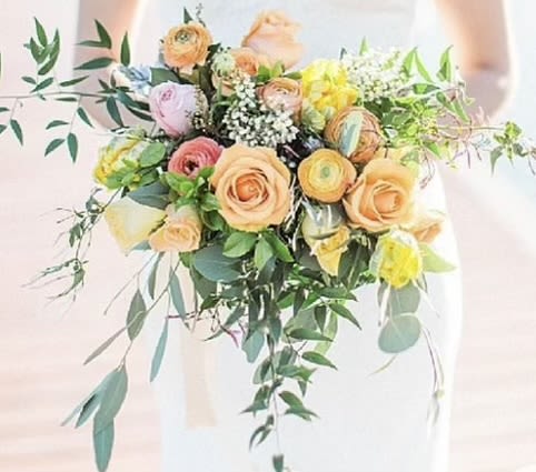 Bouquet of peach, pink, and yellow flowers with trailing greenery