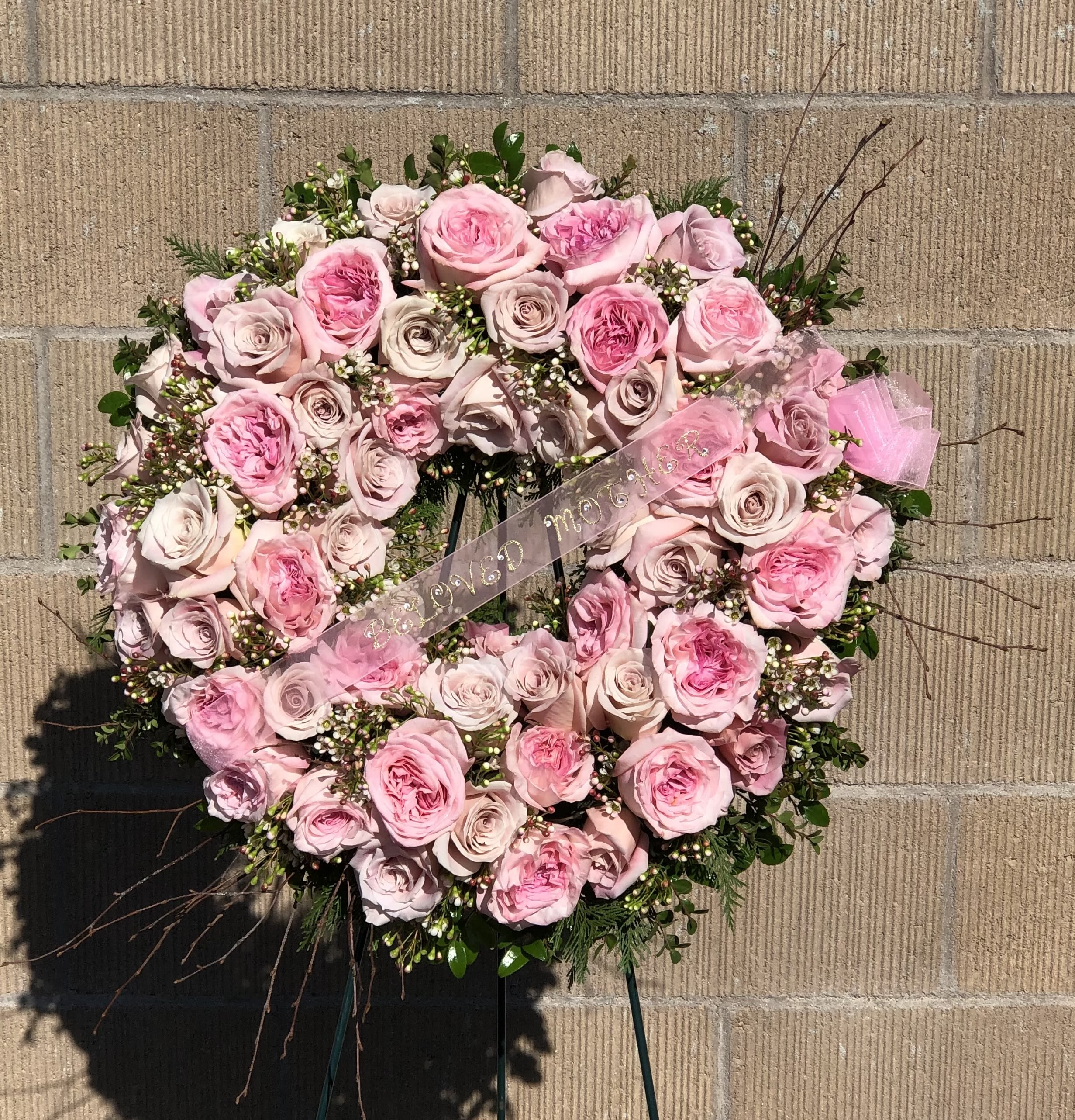 Heart-shaped pink rose wreath with a ribbon on a stand