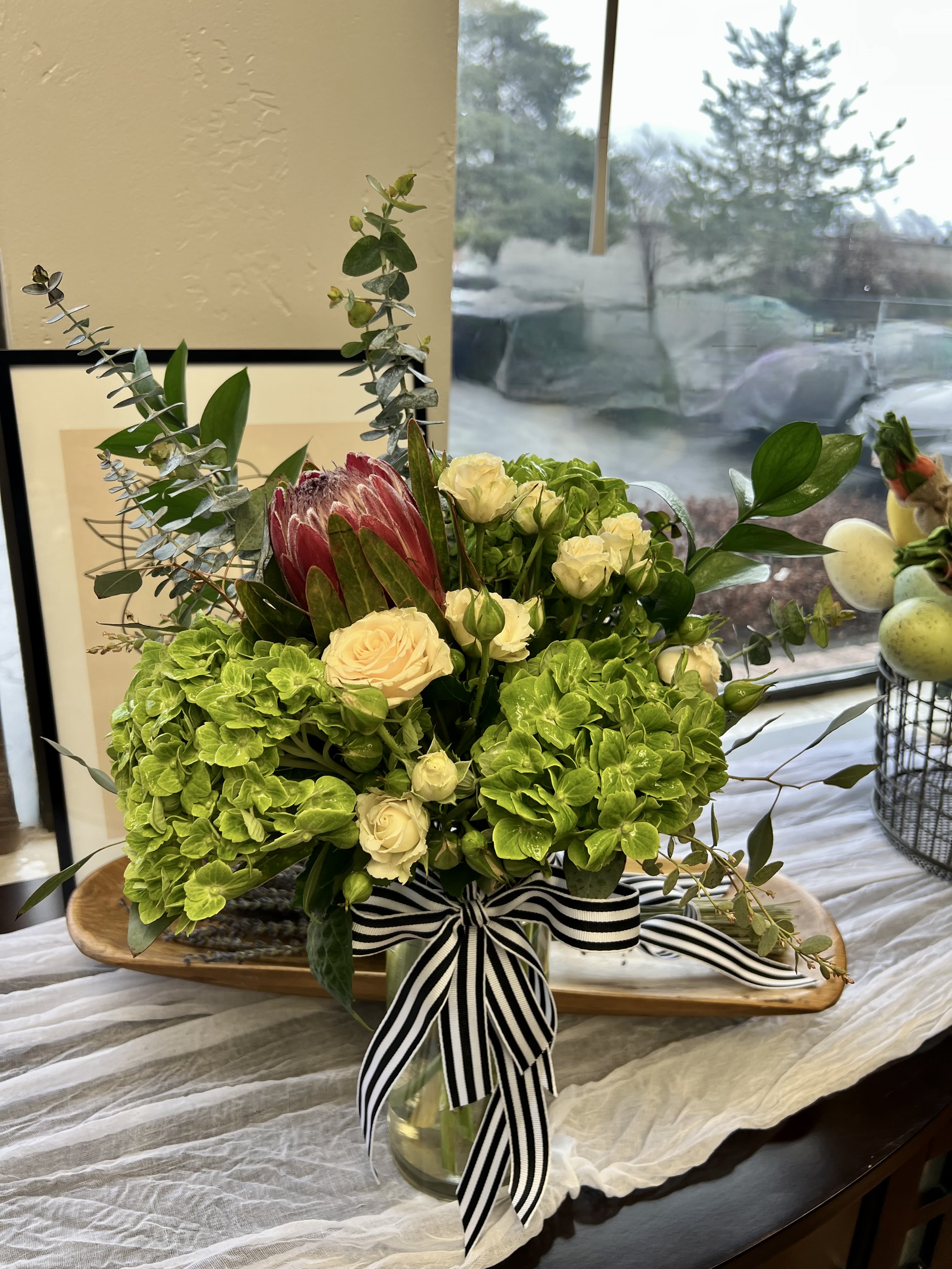 Bouquet of green hydrangeas, cream roses, and a pink protea in a glass vase