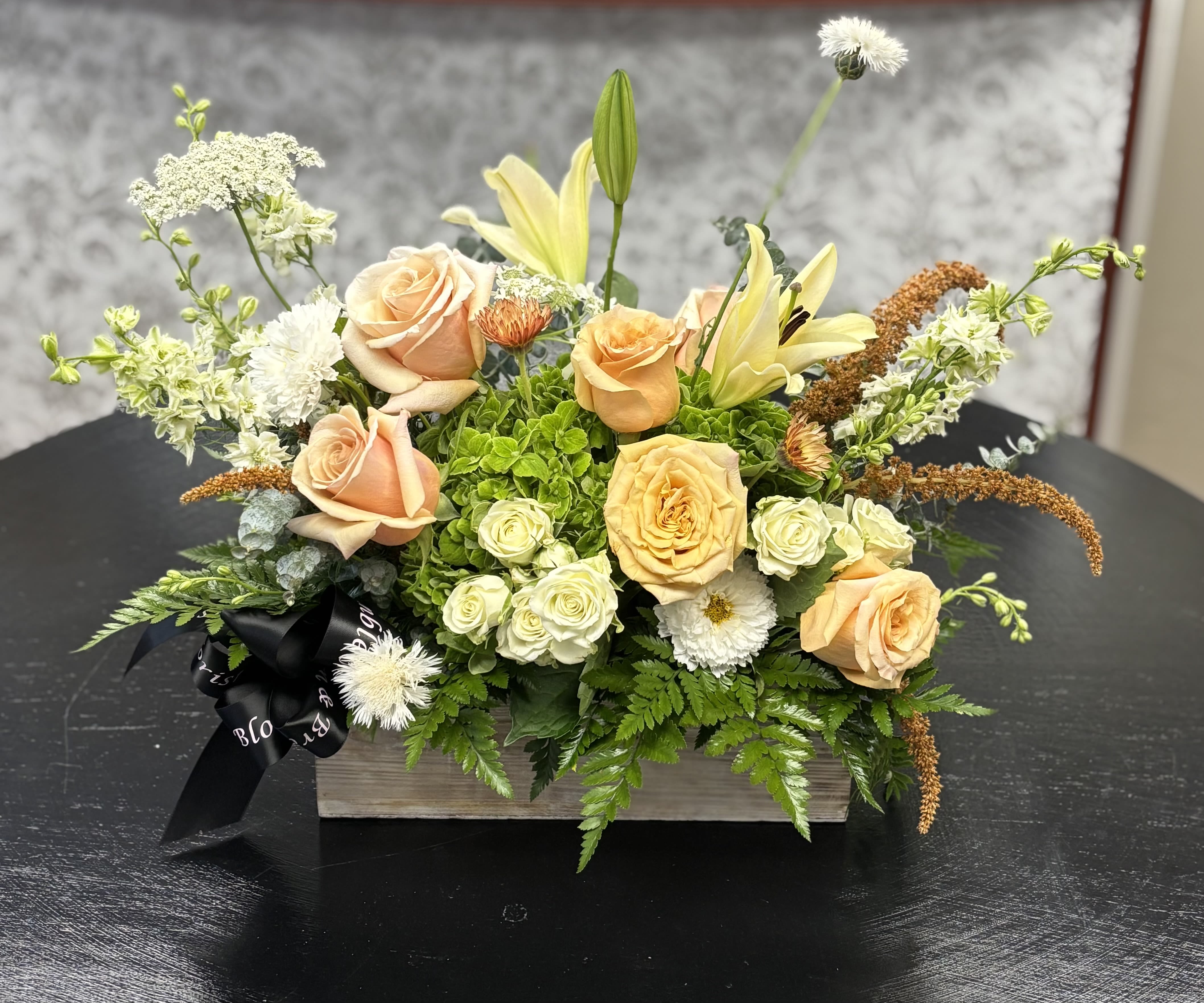 Peach roses and pale lilies arranged in a wooden box